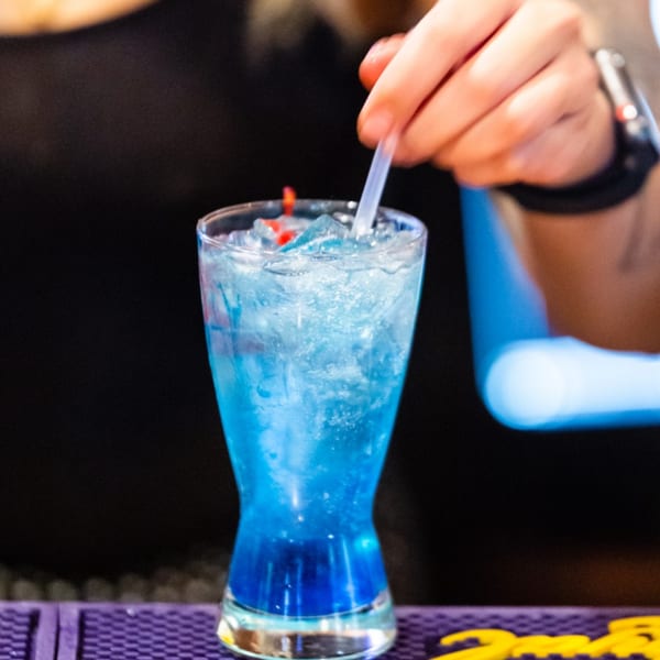 Bartender stirring a vibrant blue cocktail with ice and a red garnish at Tsubaki Restaurant.