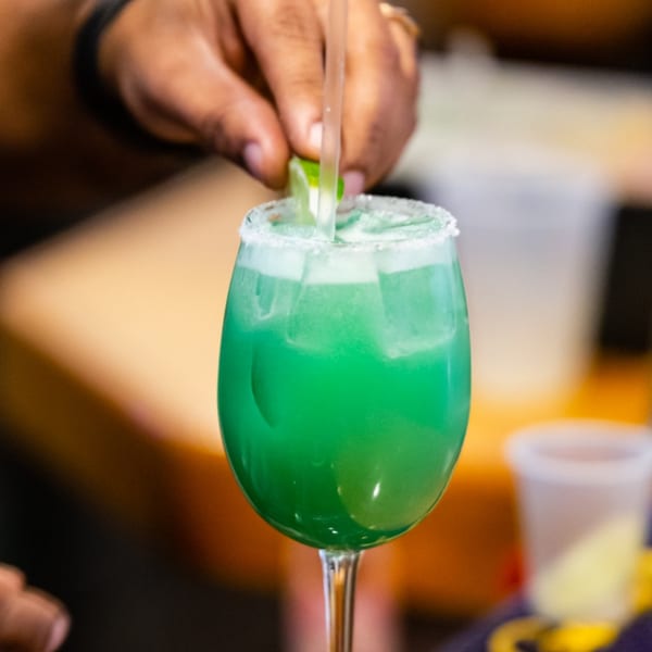 A hand garnishes a vibrant green cocktail with a lime wedge at Tsubaki Restaurant.