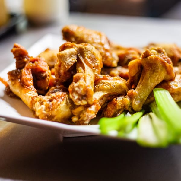 A plate of golden-brown chicken wings with a sweet glaze, garnished with fresh celery sticks.